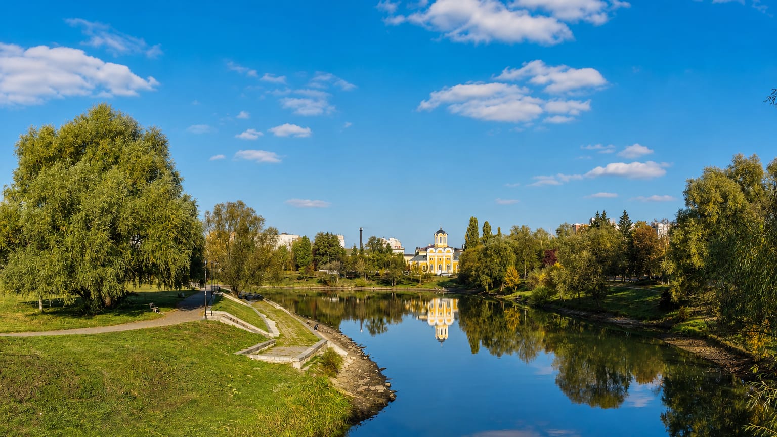 Riverside park in Chernihiv, Ukraine, with a white golden-domed church reflected in a calm pond among autumn trees
