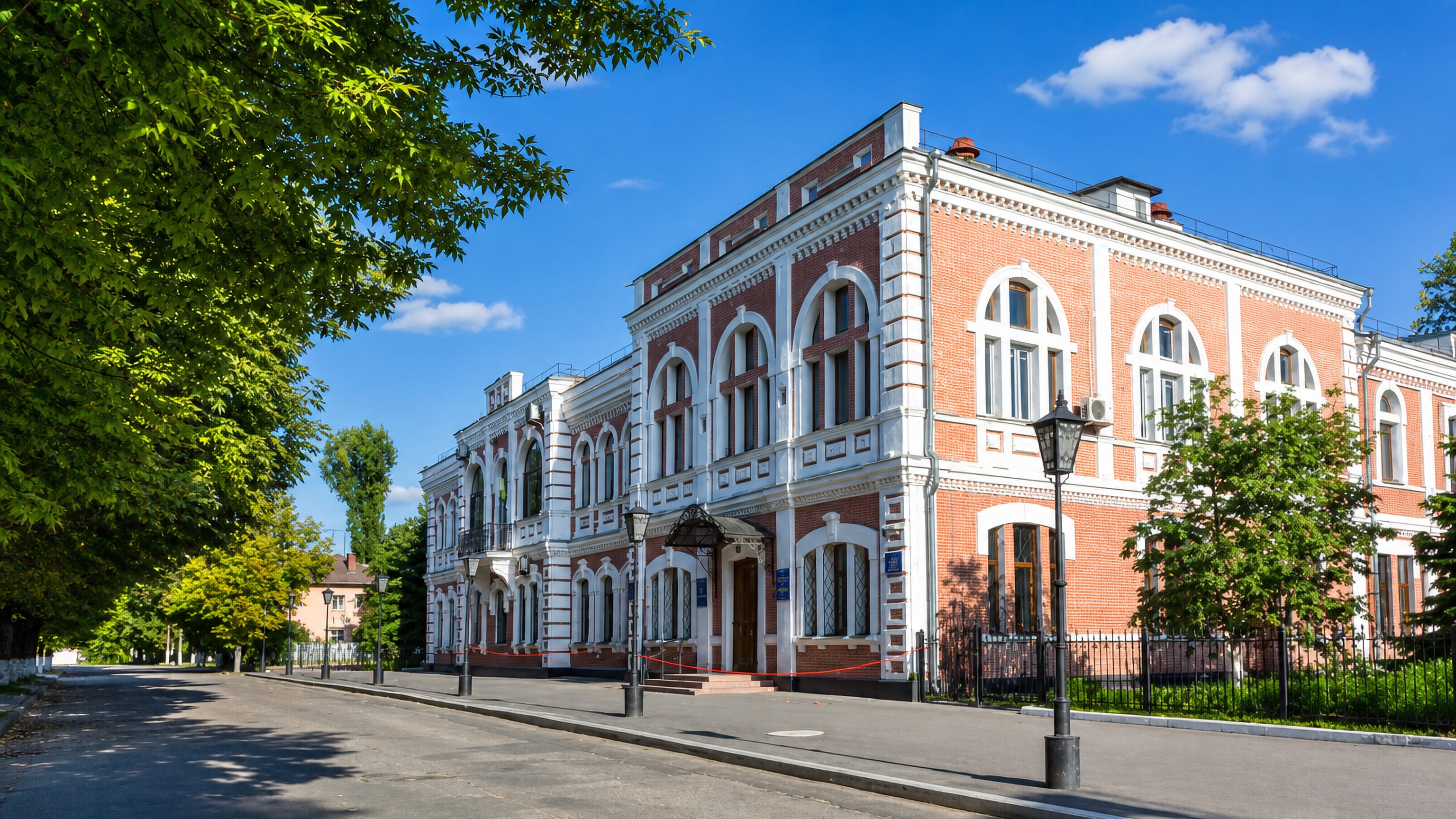 Red-brick and white 19th-century civic building on a tree-lined street in central Pavlohrad, Ukraine.