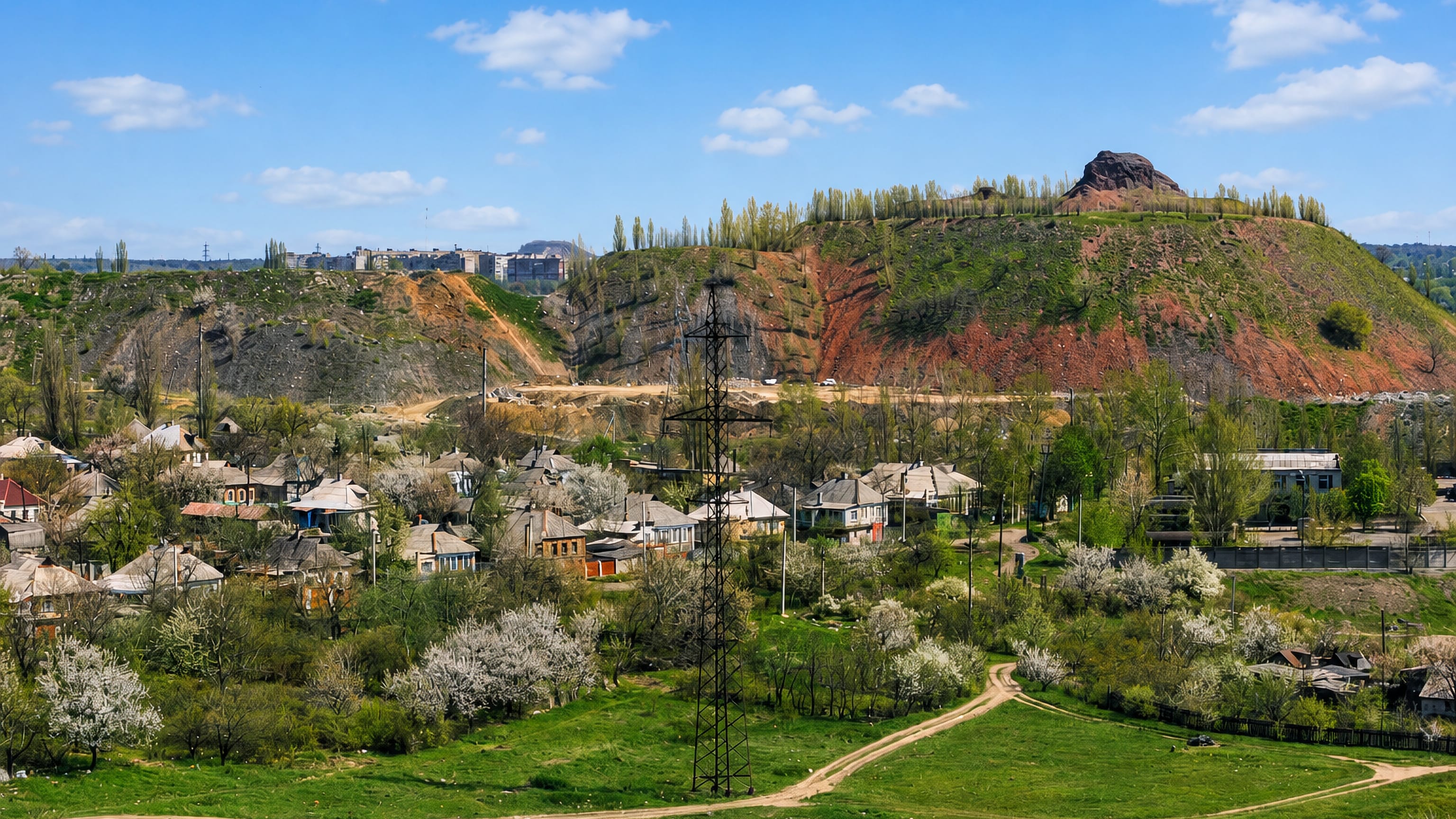 Low-rise houses in spring blossom below a green mine spoil tip on the edge of Makiyivka, Ukraine.