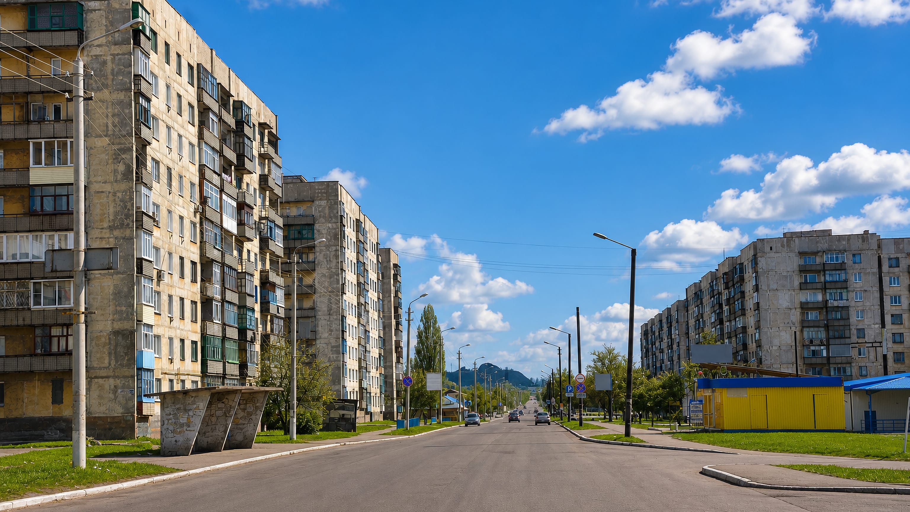 Soviet-era apartment blocks lining a quiet sunlit street in Snizhne, Donetsk region, with a spoil tip beyond.