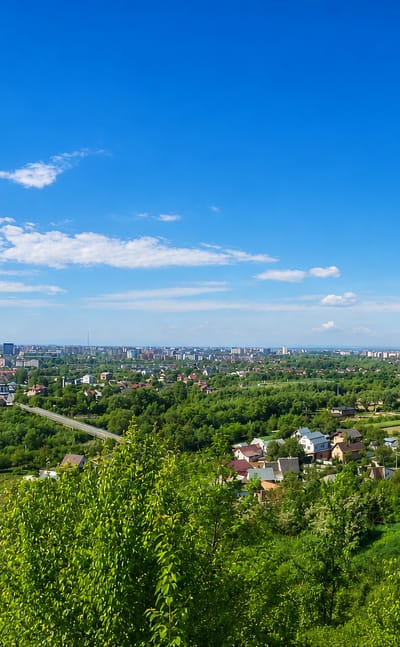 Aerial view over the green outskirts of Ivano-Frankivsk, Ukraine, toward distant apartment blocks