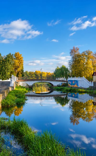 Autumn park scene in Khmelnytskyi, Ukraine, with a small stone bridge over a calm reflecting river lined with willows