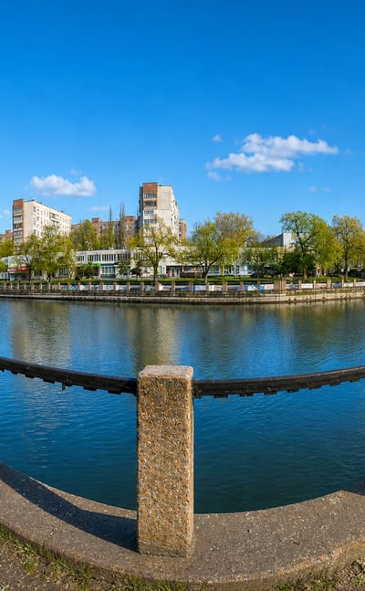 Riverside embankment in Kropyvnytskyi, Ukraine, curving past apartment blocks and a bridge under a blue sky.