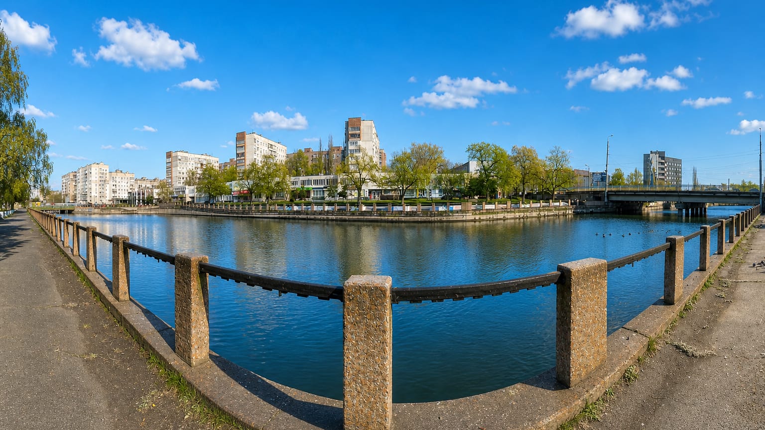 Riverside embankment in Kropyvnytskyi, Ukraine, curving past apartment blocks and a bridge under a blue sky.