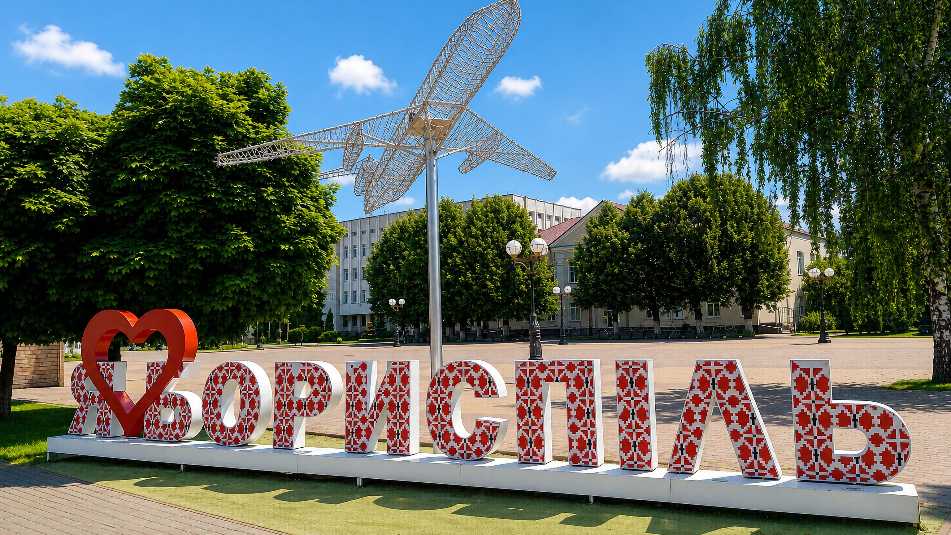 Letter sculpture spelling Boryspil in embroidery patterns beside a wireframe aeroplane monument on the city square.