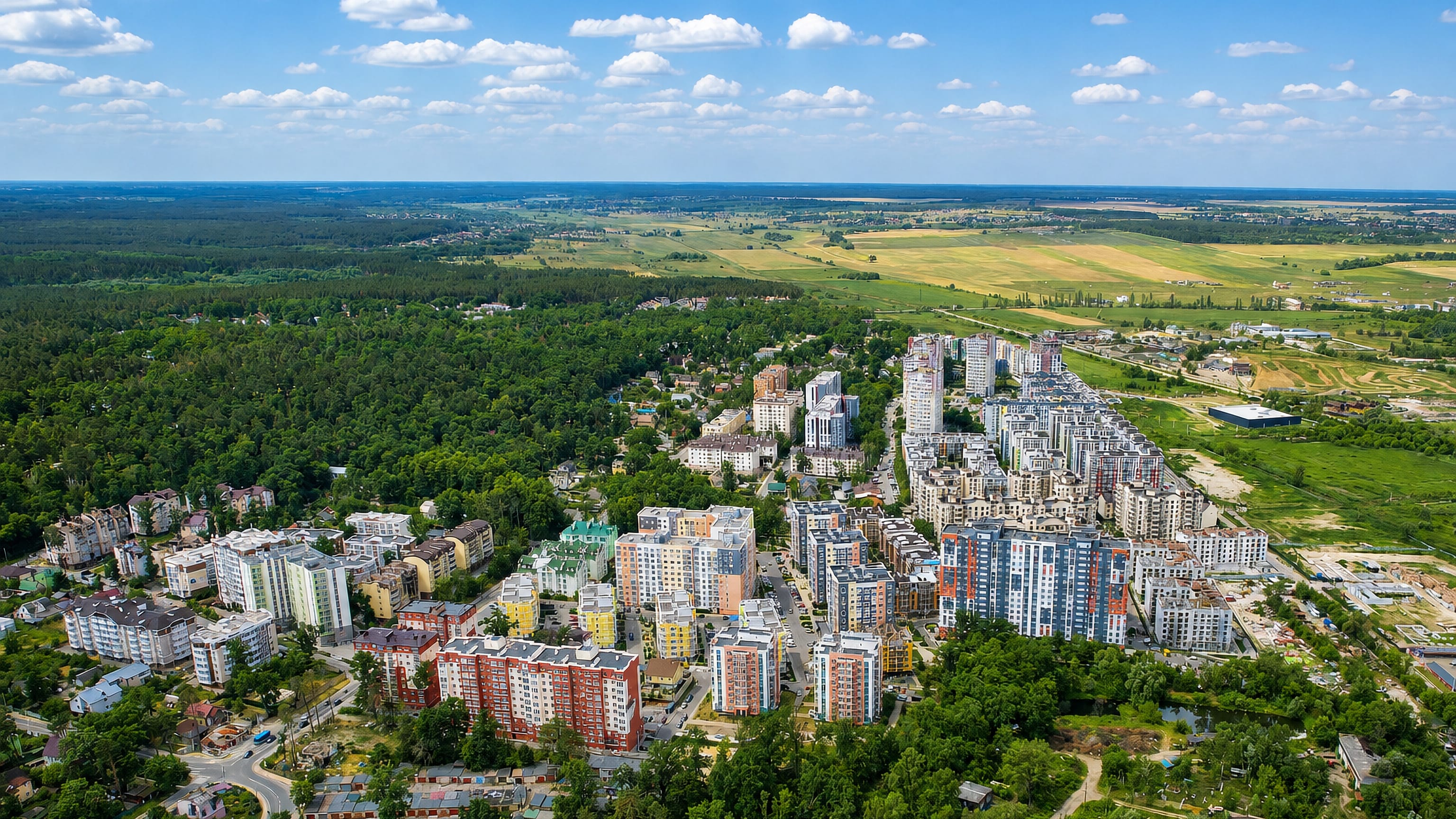 Aerial view of Irpin's colourful new apartment blocks set among pine forest at the edge of open fields.