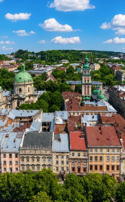 Lviv old town rooftops with the green dome of the Dominican Church and a historic bell tower on a sunny day.