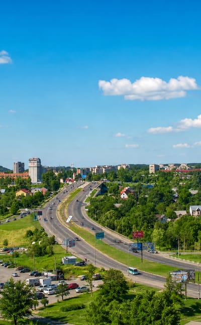 Sunny residential view of Sykhiv, a Lviv district, with mid-rise blocks, a highway and green wooded suburbs.
