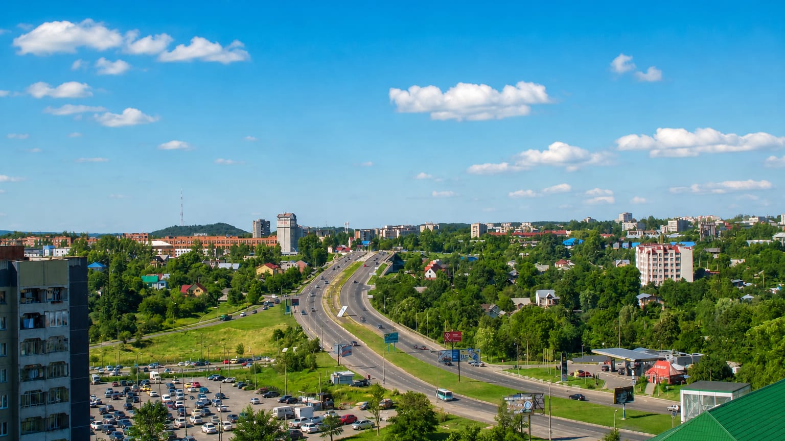 Sunny residential view of Sykhiv, a Lviv district, with mid-rise blocks, a highway and green wooded suburbs.