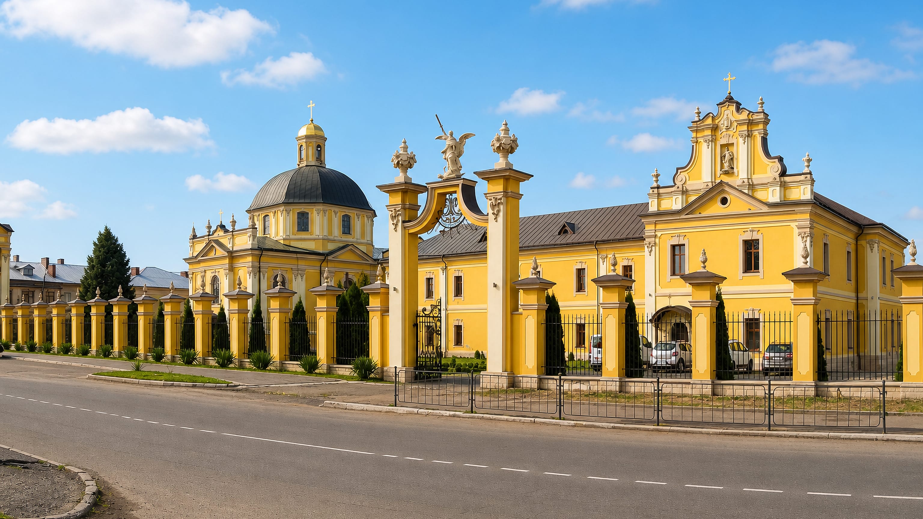 The yellow baroque monastery complex and gate in Sheptytskyi, Ukraine, seen from the roadside.