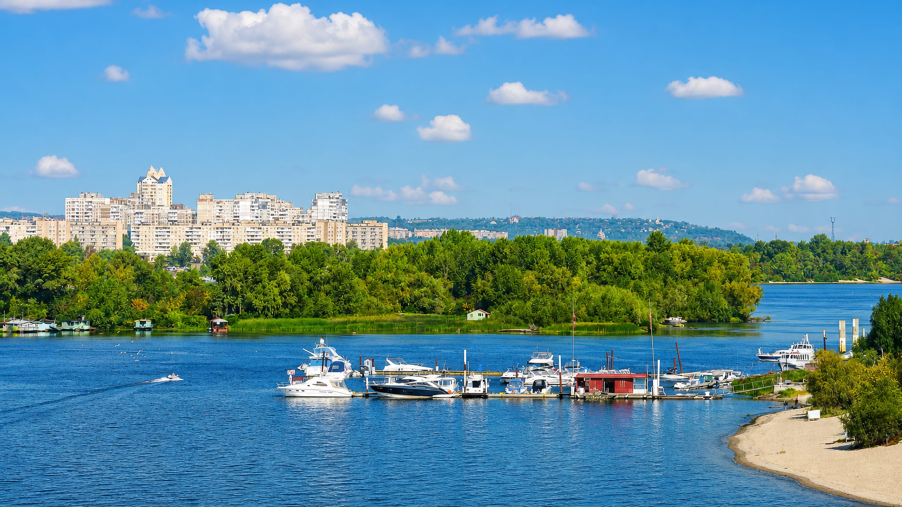Dnieper river marina and Soviet-era apartment blocks of Kyiv's Desnianskyi District under summer skies.