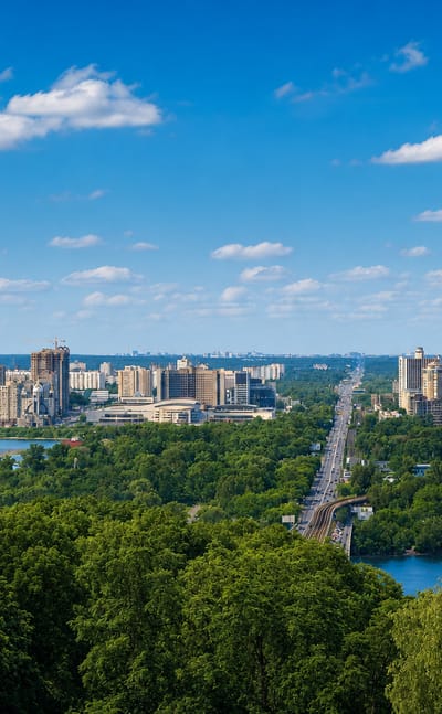 Aerial panorama of Kyiv's Pecherskyi District with forested hills and the Dnieper River in the distance.