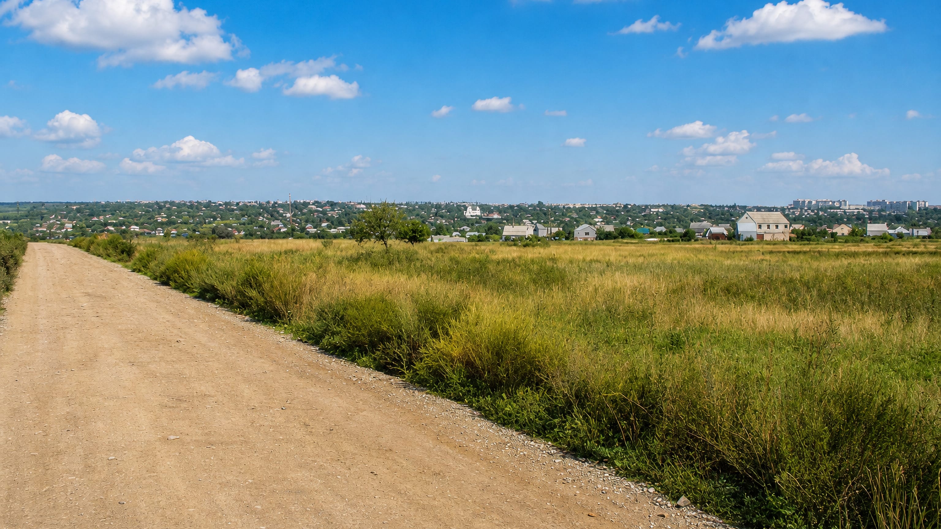Gravel track through summer grassland leading toward the low skyline of Pervomaysk, Ukraine.