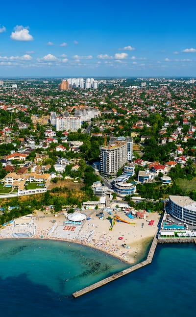 Aerial view of Odesa's Black Sea coastline with a curved beachfront resort, sandy beach and leafy suburbs.
