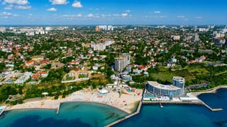 Aerial view of Odesa's Black Sea coastline with a curved beachfront resort, sandy beach and leafy suburbs.