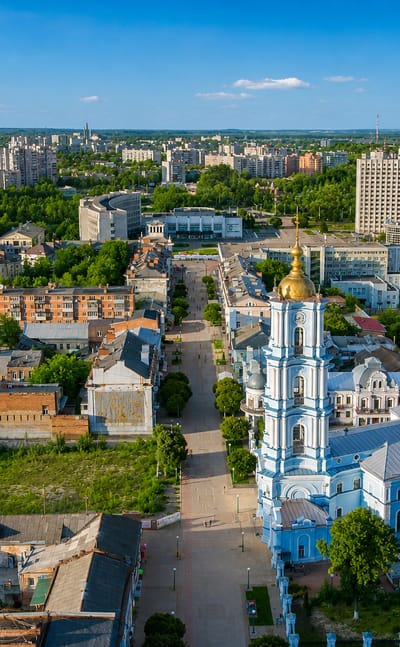 Aerial view of Sumy, Ukraine, with the blue-and-gold Transfiguration Cathedral rising above a tree-lined pedestrian street.