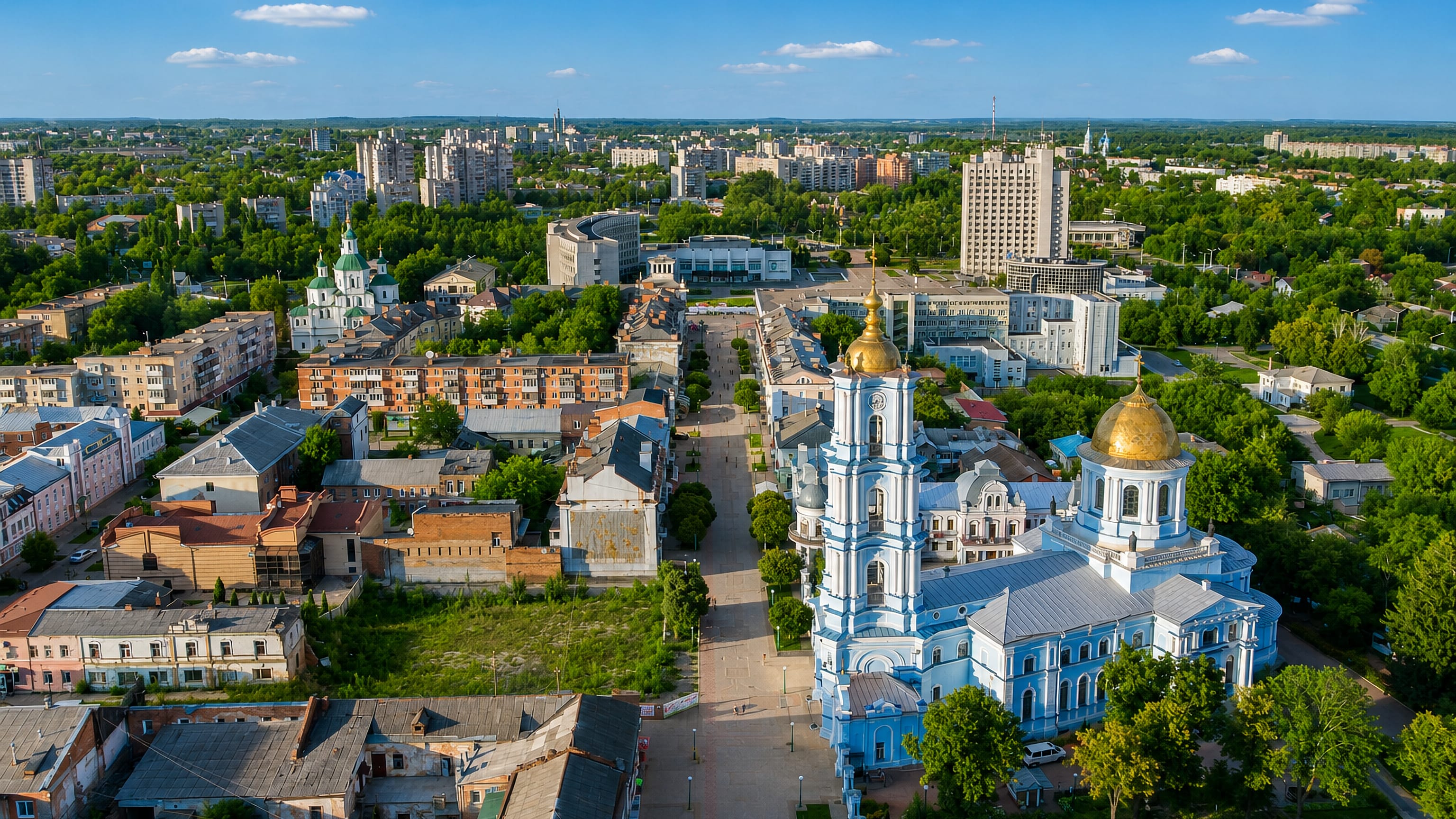 Aerial view of Sumy, Ukraine, with the blue-and-gold Transfiguration Cathedral rising above a tree-lined pedestrian street.