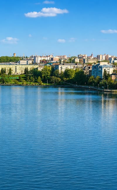 Ternopil's skyline and green church domes seen across the calm Ternopil Pond with a riverside boulevard