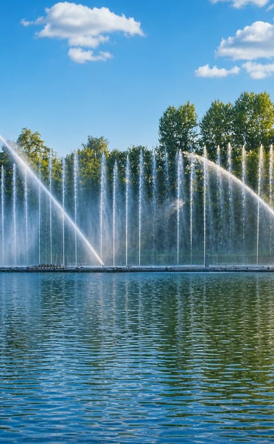 Vinnytsia's Roshen floating fountain shooting tall water jets over the Southern Bug river beside green trees