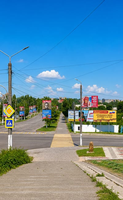 Wide boulevard in Melitopol, Ukraine, lined with billboards and street lamps under a clear blue sky.