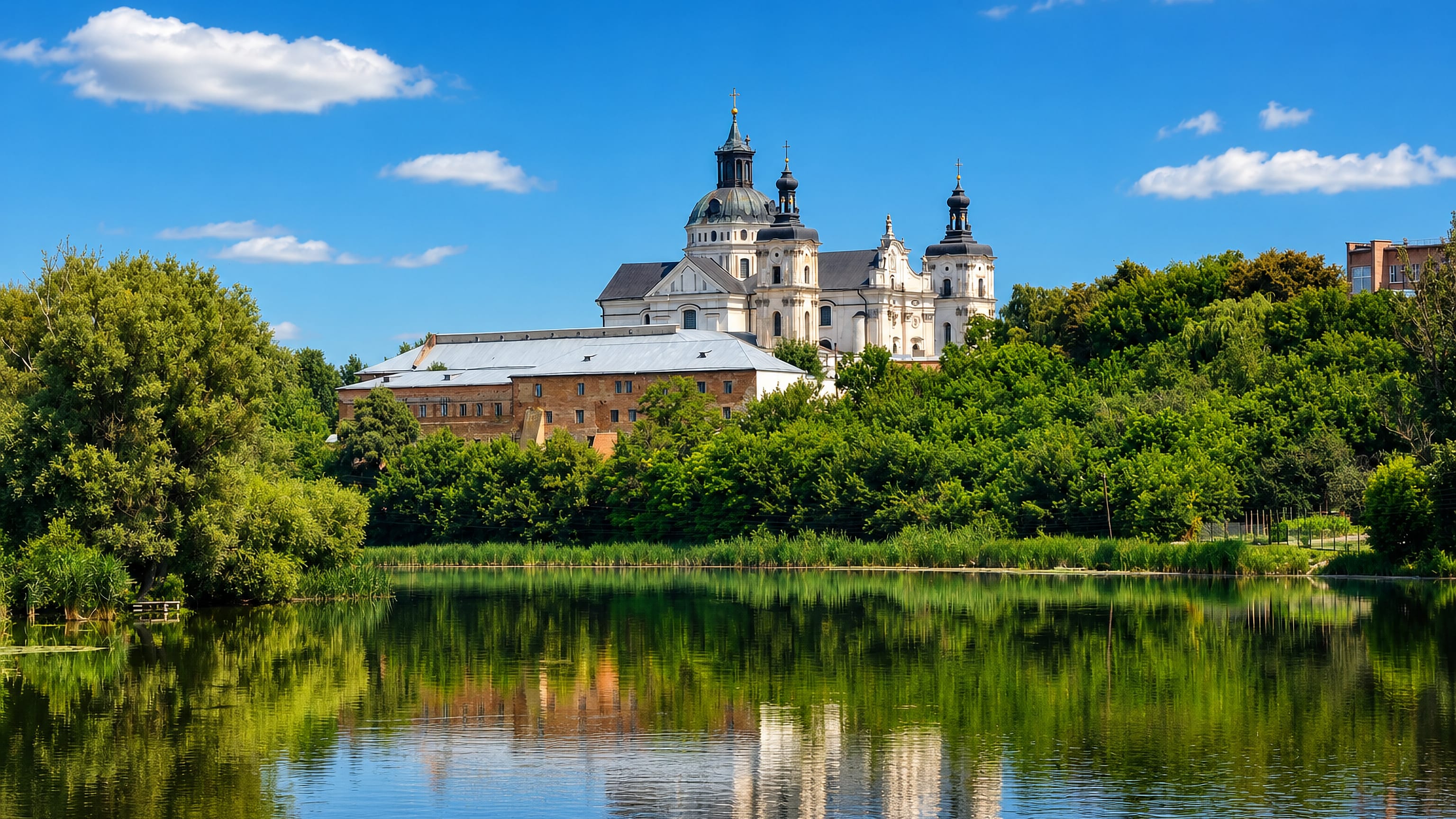 The baroque Carmelite monastery of Berdychiv, Ukraine, above wooded banks reflected in the Hnylopiat River.