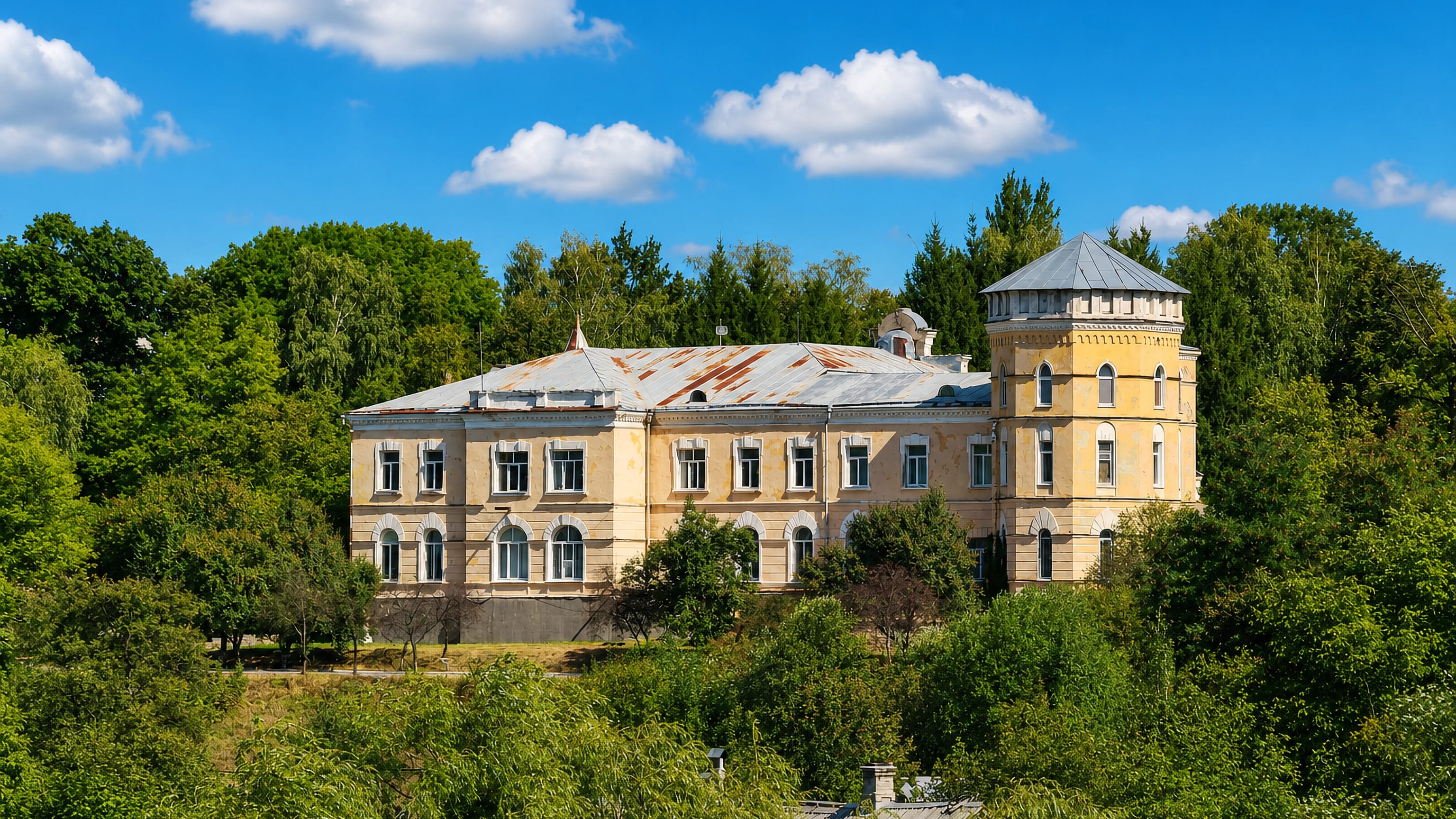 Yellow neoclassical manor with a corner turret standing above wooded slopes in Zvyahel, Zhytomyr region, Ukraine.
