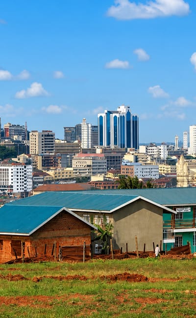 Kampala's hilltop skyline of mid-rise towers rising beyond red-brick houses and green fields, Uganda.