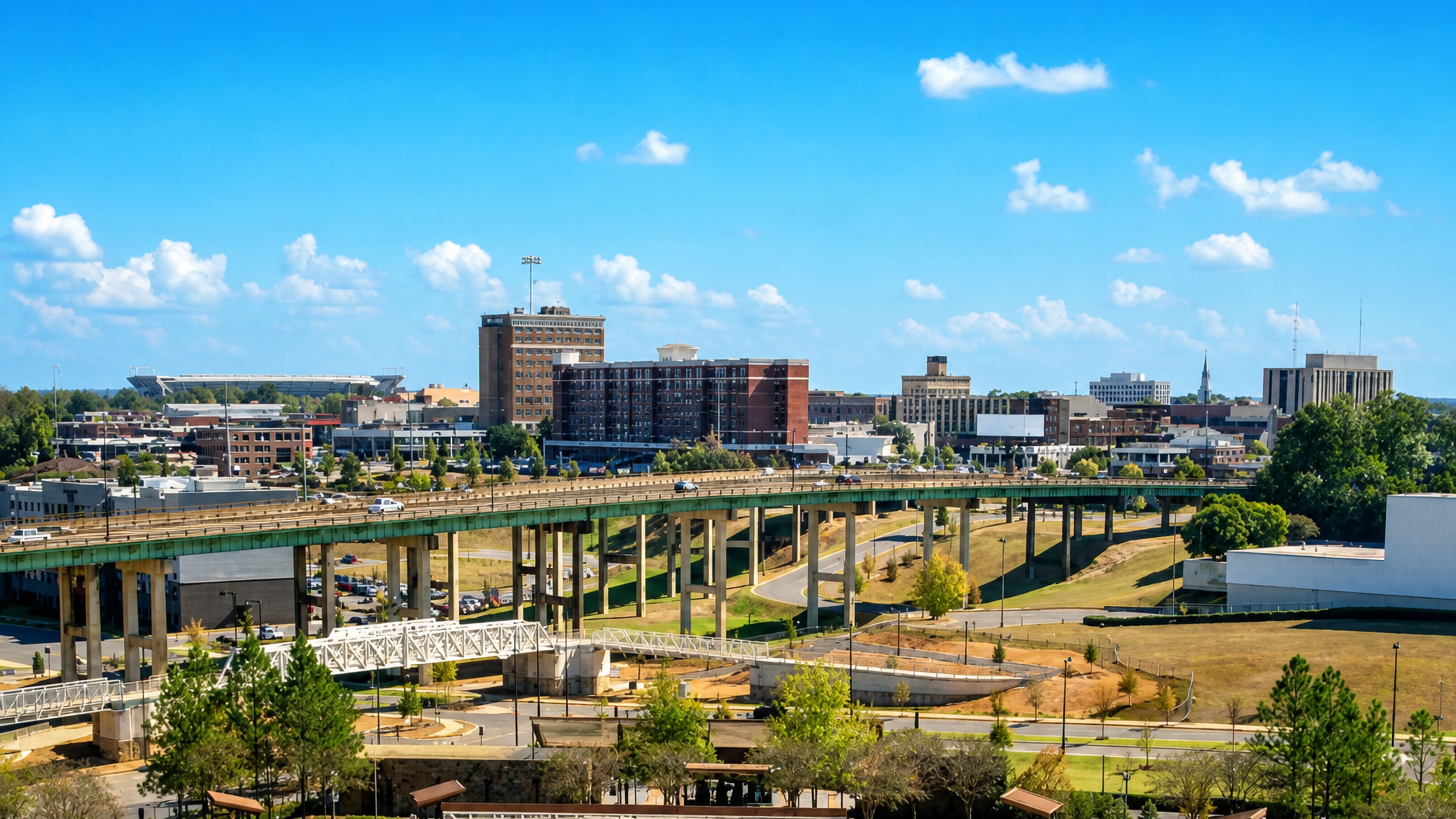 Tuscaloosa's downtown skyline behind the elevated riverfront highway, with Bryant-Denny Stadium beyond