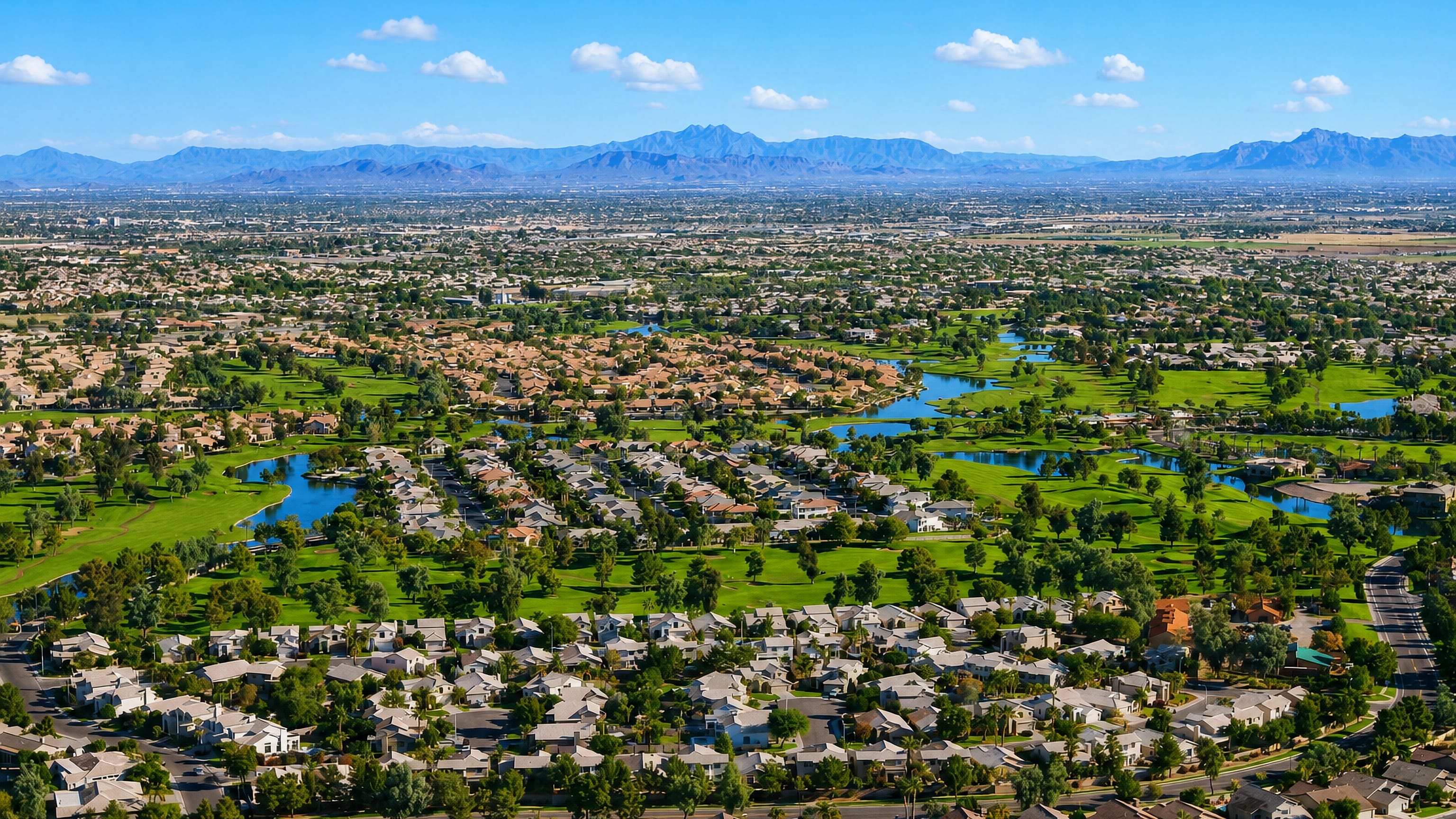 Aerial view over Chandler, Arizona, showing golf-course lakes, tiled-roof homes and distant desert peaks