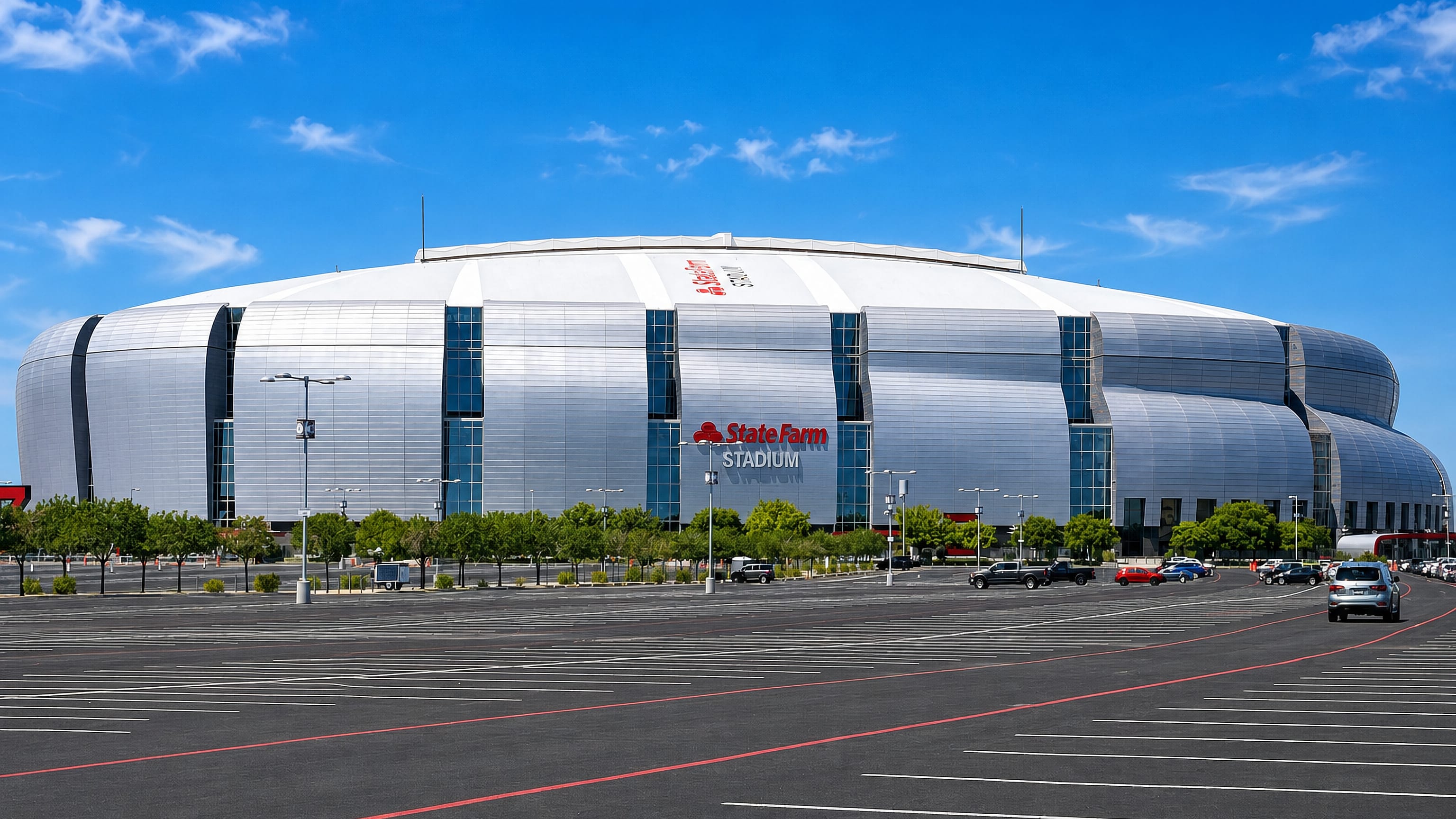 State Farm Stadium's curved silver facade above its wide empty parking lot in Glendale, Arizona.