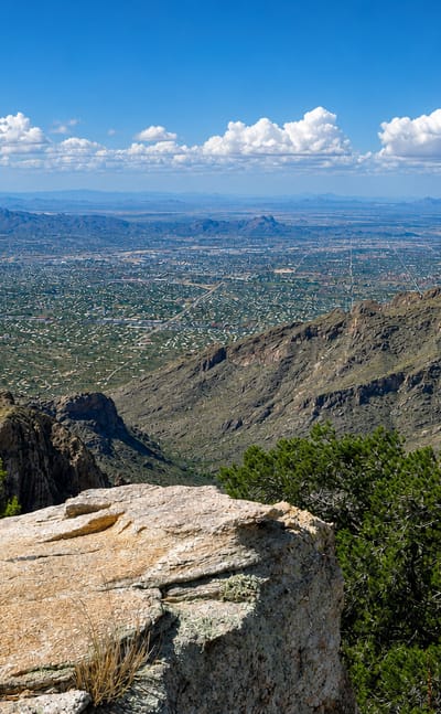Tucson's desert basin and city grid seen from the Santa Catalina Mountains under a cloud-dotted sky