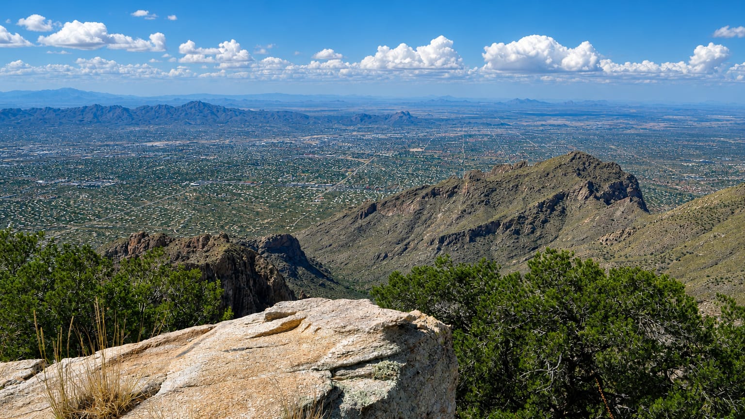 Tucson's desert basin and city grid seen from the Santa Catalina Mountains under a cloud-dotted sky
