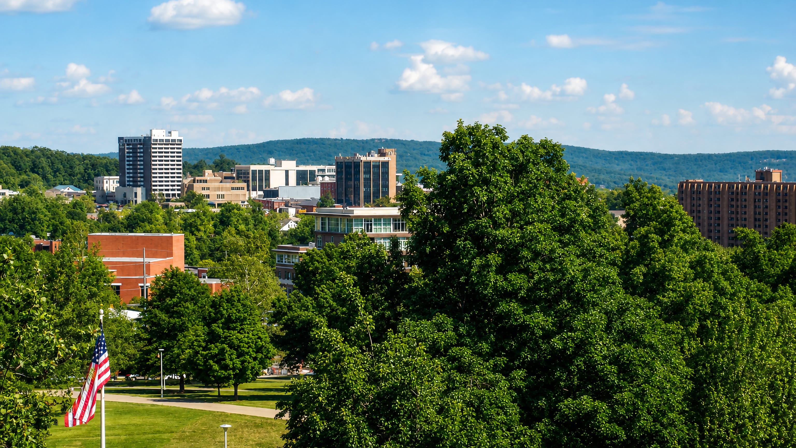 Downtown towers rise above summer tree canopy and the Ozark hills in Fayetteville, Arkansas.