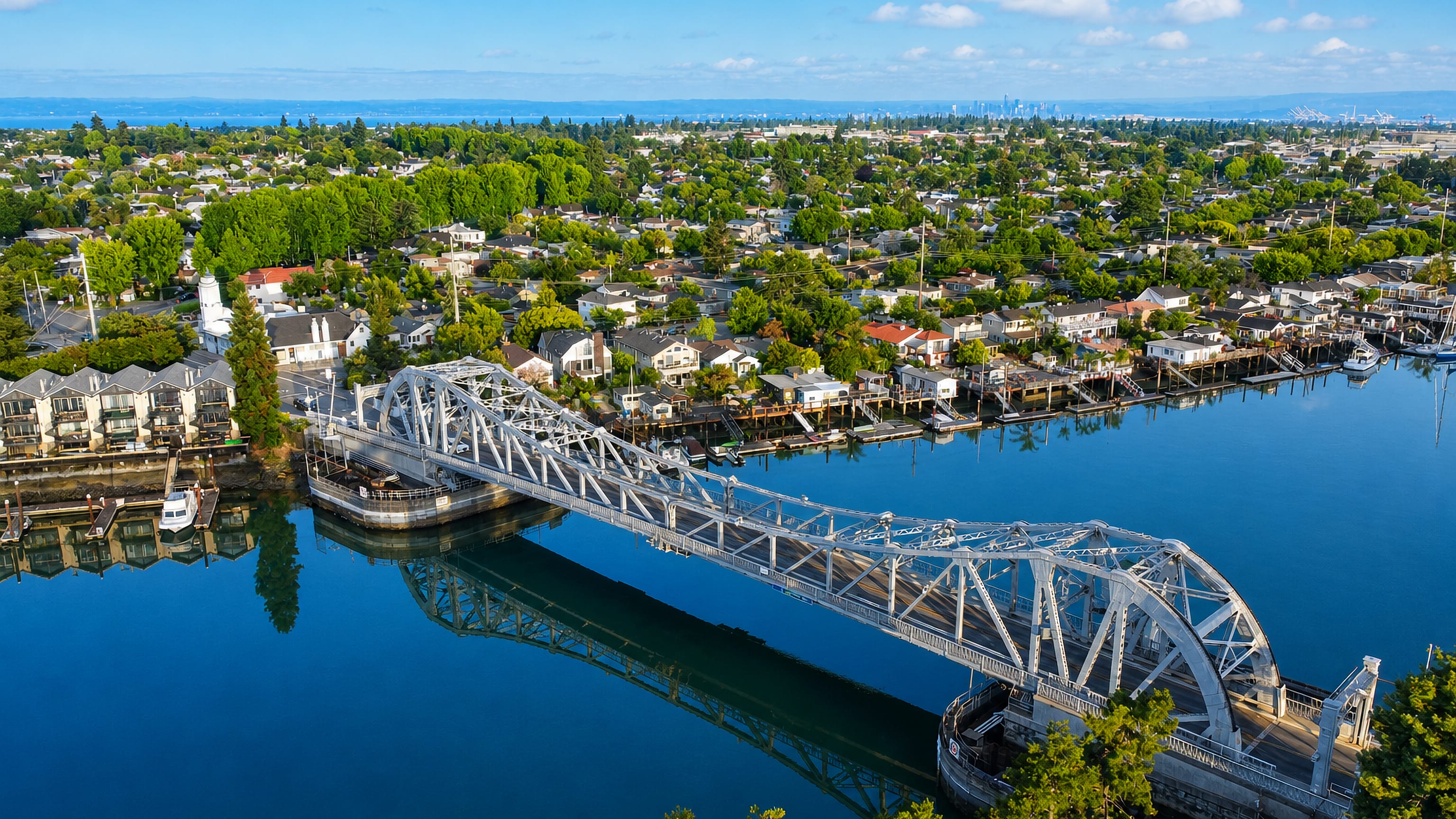 Alameda, California, from the air with a steel truss bridge over the estuary and the San Francisco skyline beyond.