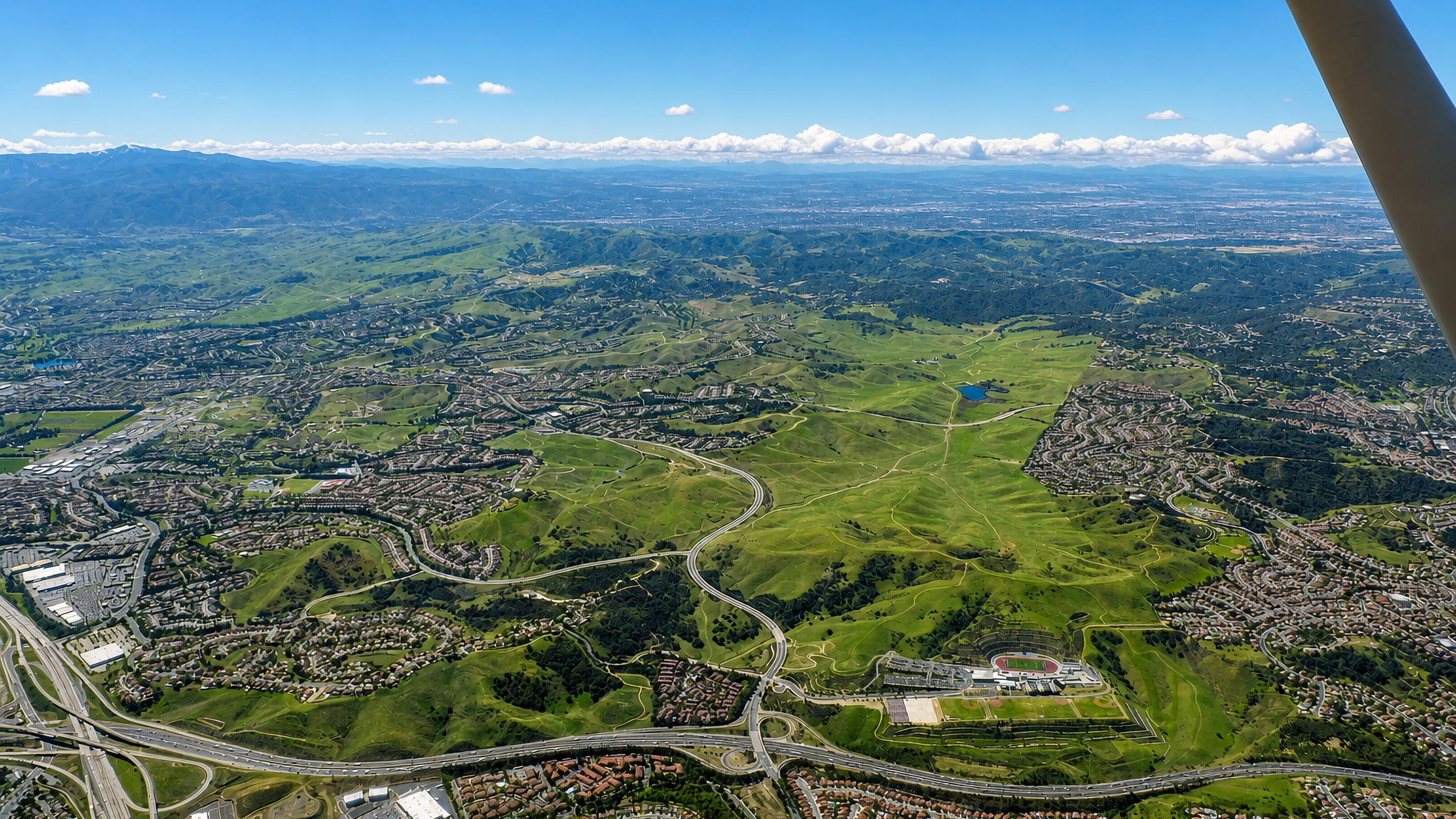 Aerial view of Chino Hills, California, its suburban tracts spread across green rolling hills beside the freeway.