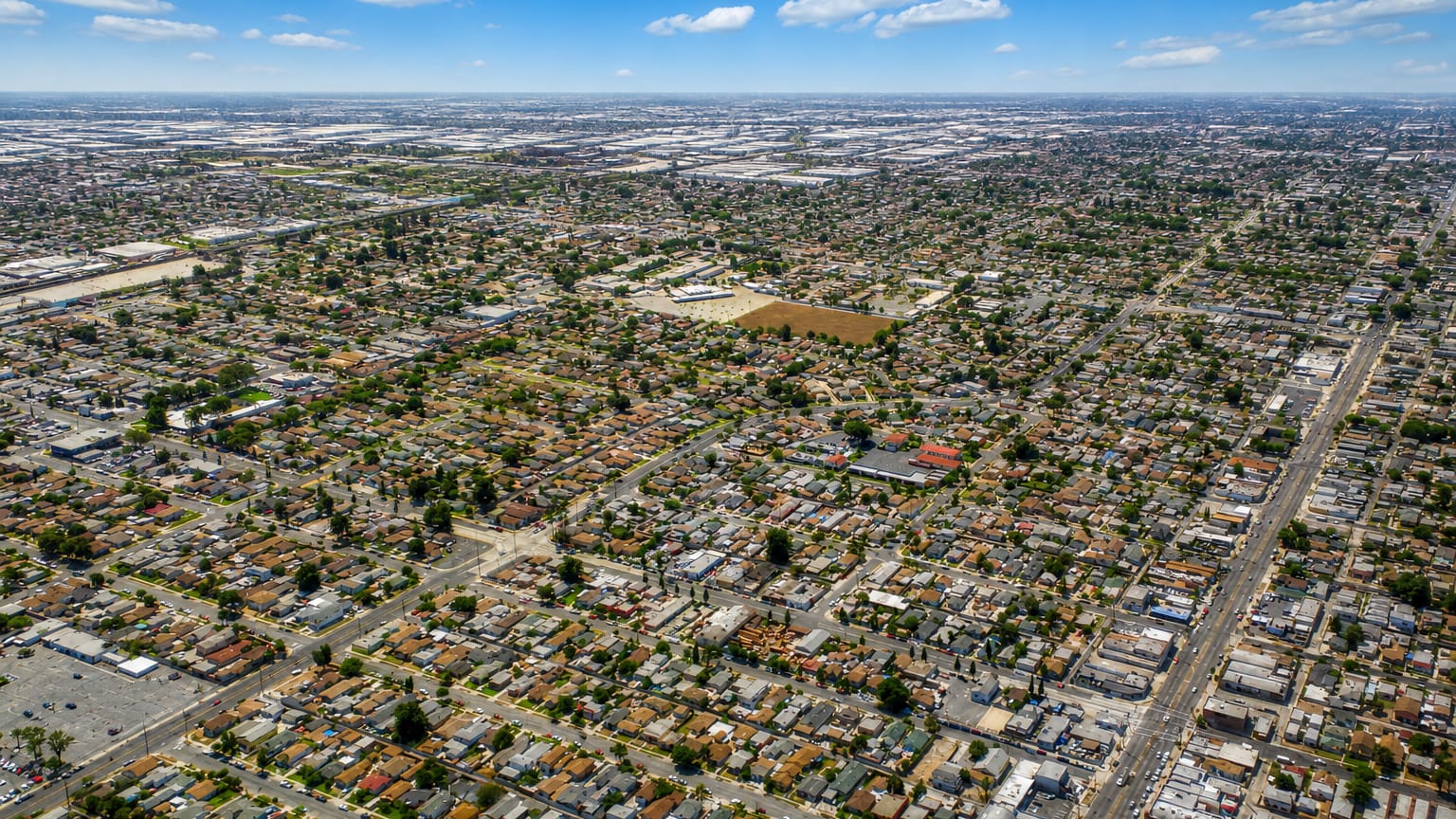 Aerial view over Compton, California, a flat grid of homes stretching to distant warehouse districts