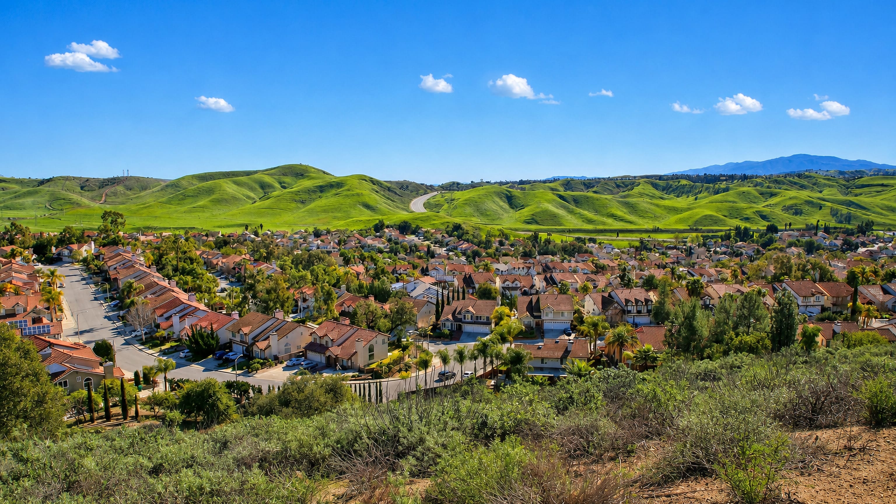 Tile-roofed hillside neighbourhoods of Diamond Bar, California, below green rolling hills under a clear sky.