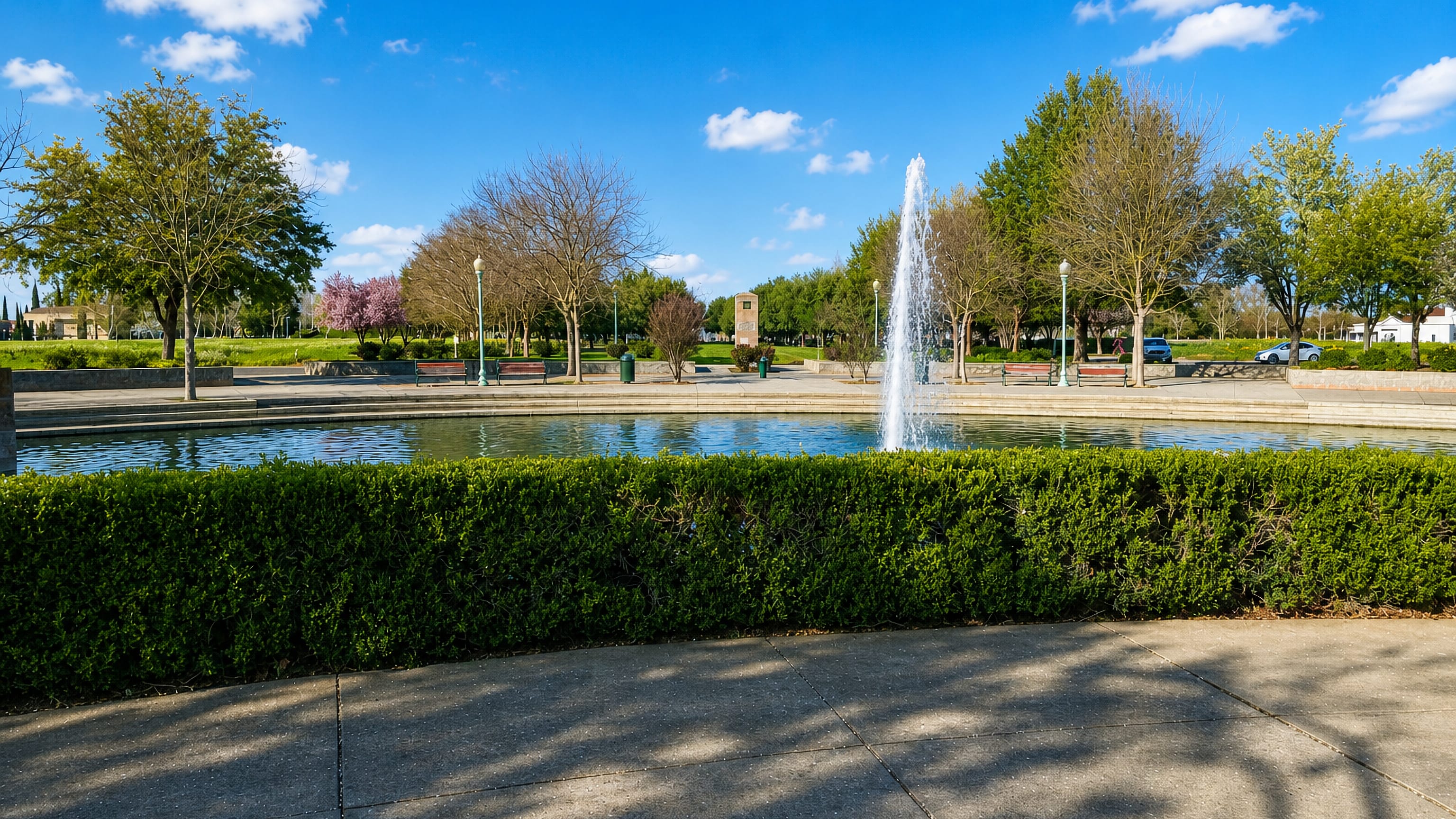 Fountain and reflecting pool in a landscaped park in Elk Grove, California, under a clear blue sky.