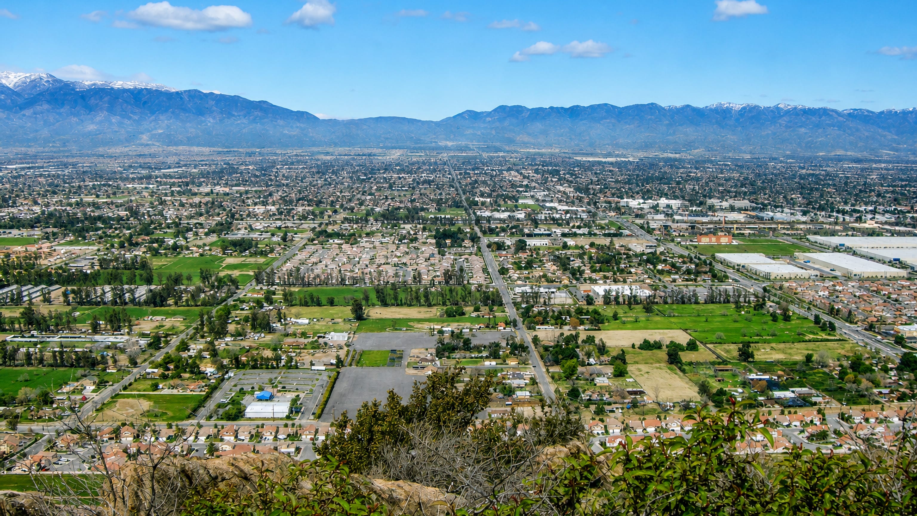 Fontana's suburban grid and warehouses spread below the snow-capped San Gabriel Mountains in California.