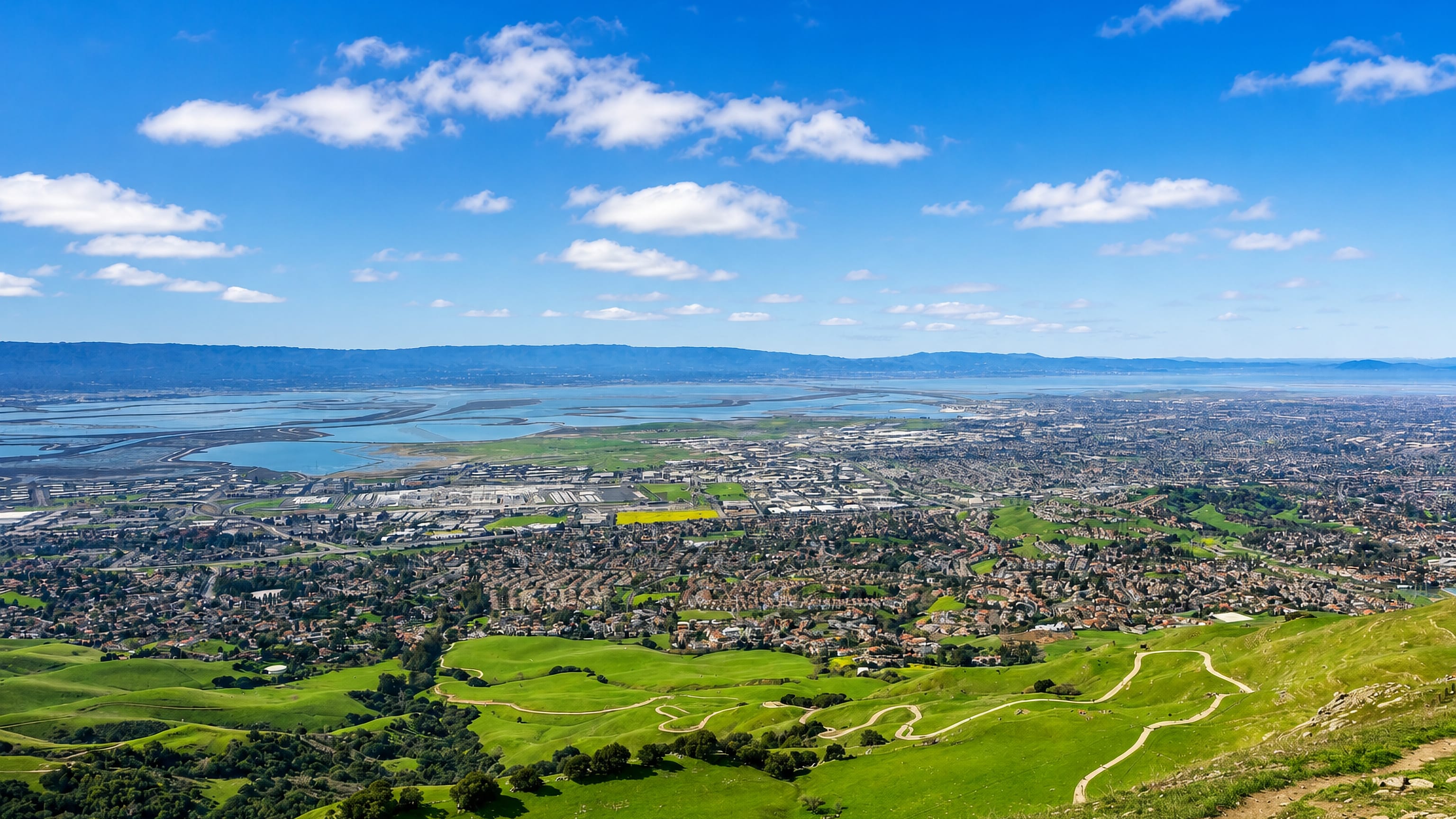 Green Mission Peak hillsides above Fremont's suburban grid, with San Francisco Bay salt ponds beyond.