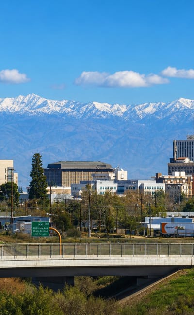 Downtown Fresno skyline with the Pacific Southwest Building tower and snow-capped Sierra Nevada beyond a freeway