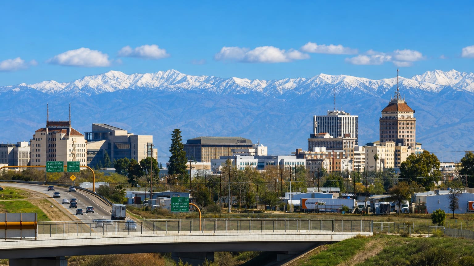Downtown Fresno skyline with the Pacific Southwest Building tower and snow-capped Sierra Nevada beyond a freeway