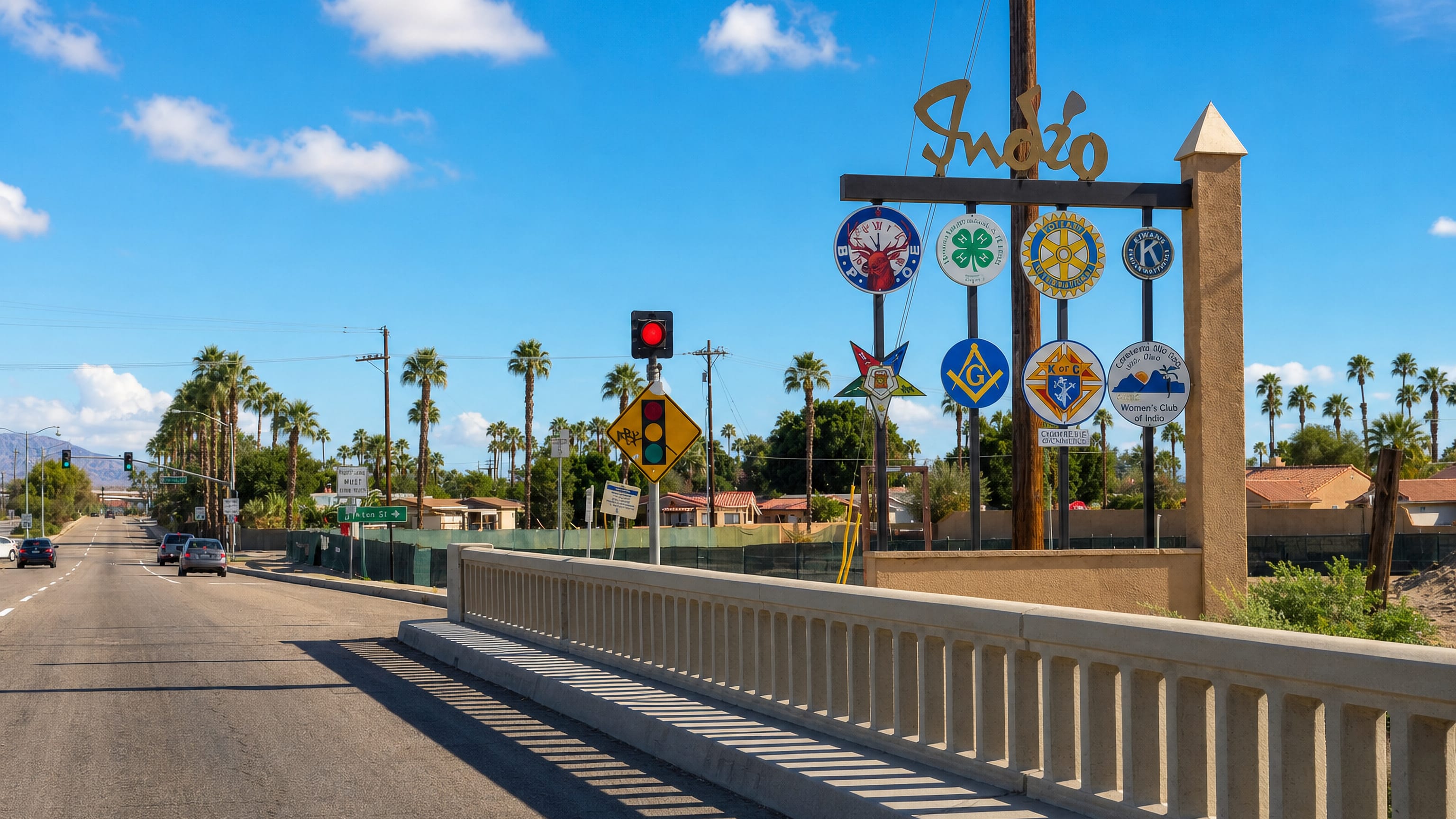 Indio, California welcome sign with service-club emblems beside a palm-lined desert boulevard and bridge railing