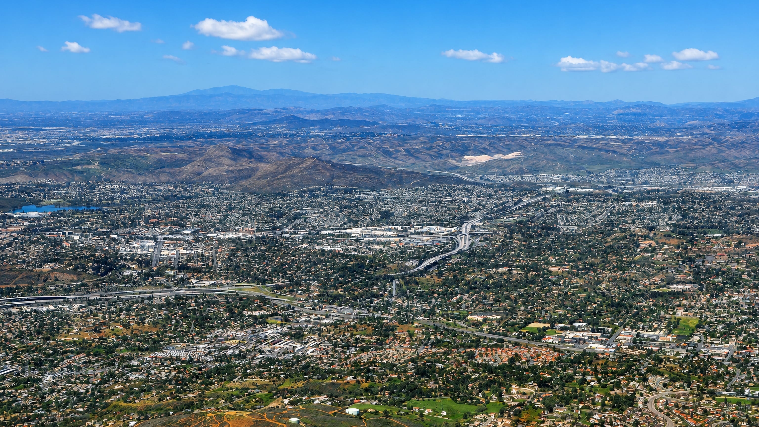 Aerial over La Mesa, California, with hillside neighbourhoods, a reservoir and freeway toward the mountains