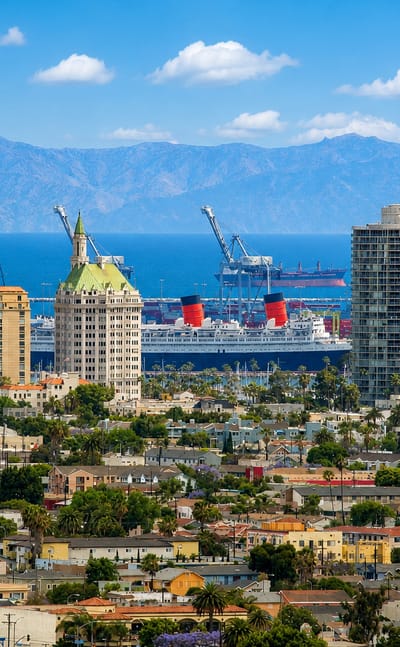 Long Beach skyline with the Queen Mary liner and port gantry cranes below mountains, California