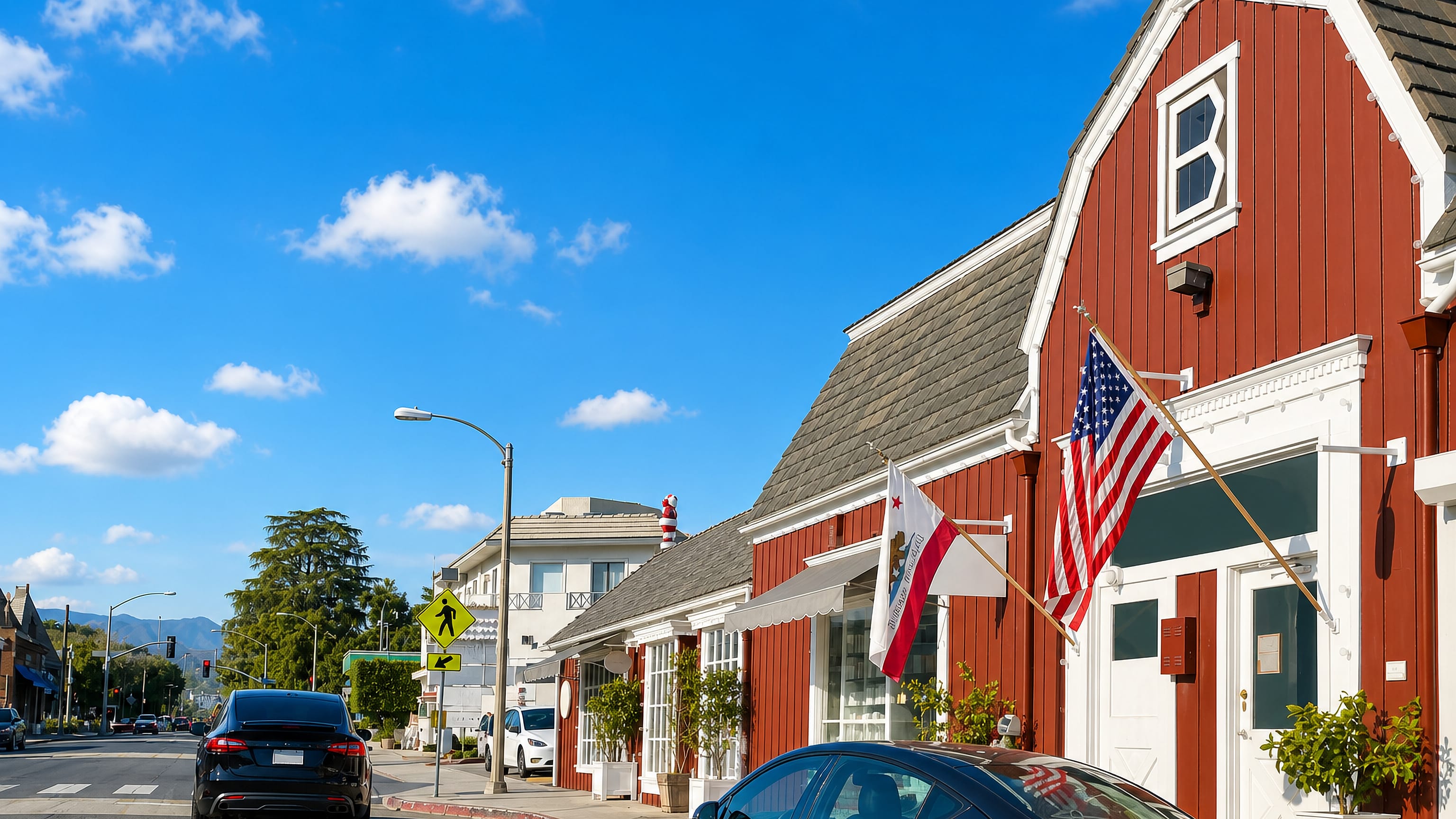 Red barn-style shops with US and California flags along a sunlit street in Brentwood, Los Angeles.