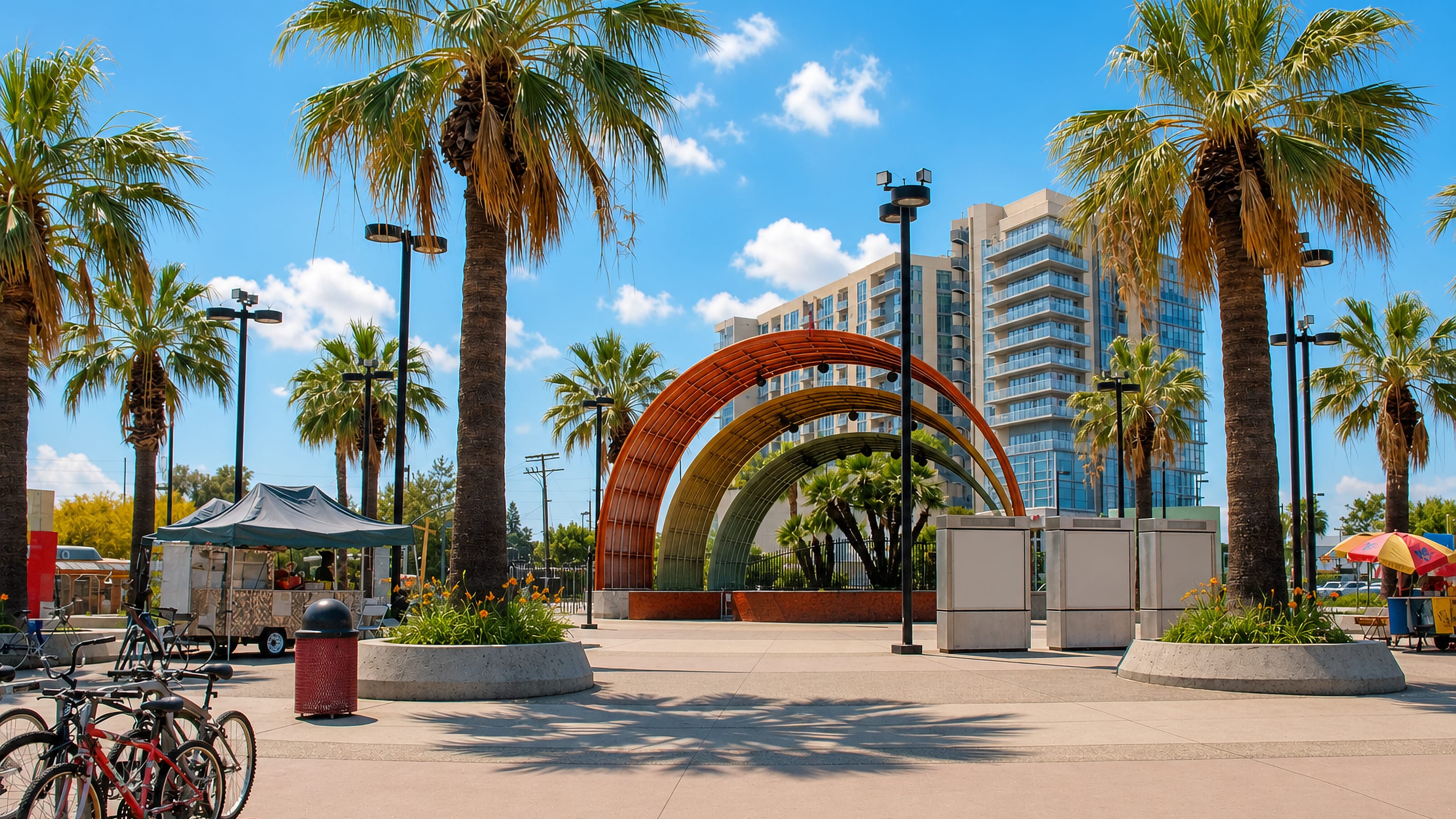 Palm-lined plaza in North Hollywood with a rainbow-hued arched shade structure and a mid-rise apartment tower
