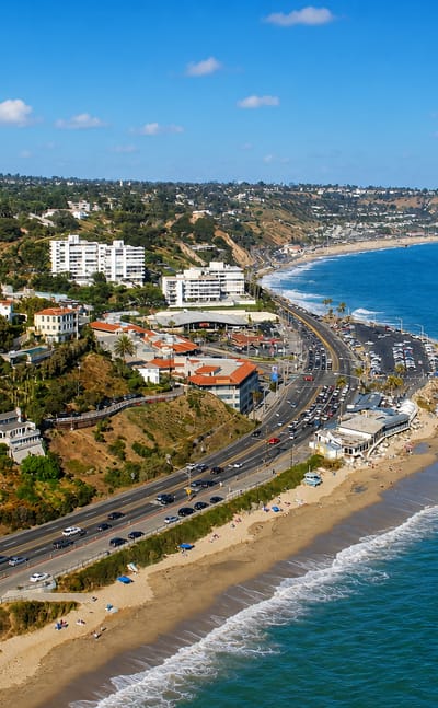 Coastal bluffs and beach along Pacific Coast Highway at Pacific Palisades, with the ocean and Santa Monica beyond