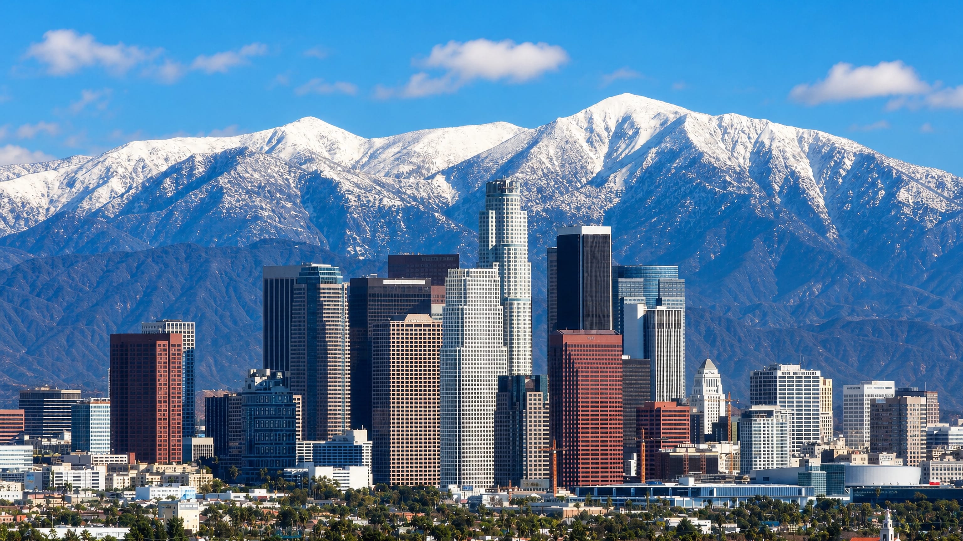 Downtown Los Angeles towers below snow-capped San Gabriel peaks, seen from the Valley Glen side of the city.