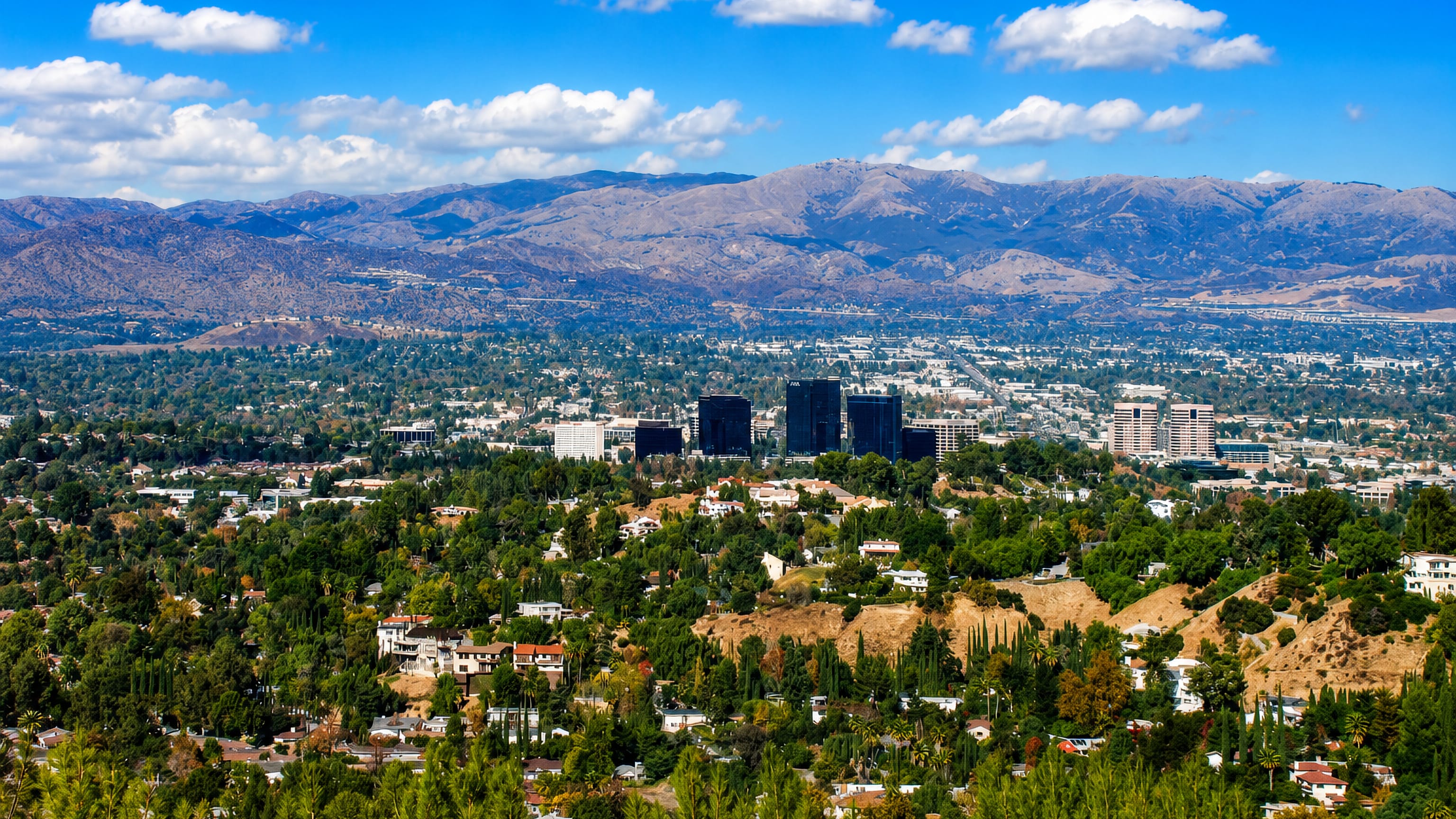 Warner Center towers rising above leafy hillside homes in Woodland Hills, Los Angeles, with the Santa Susana Mountains